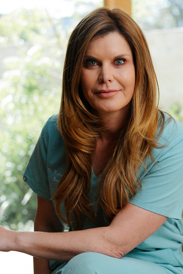 Woman in teal outfit sitting indoors with a blurred natural background