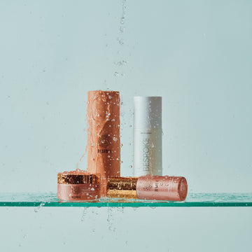 Three skincare products on a glass shelf with a light blue background