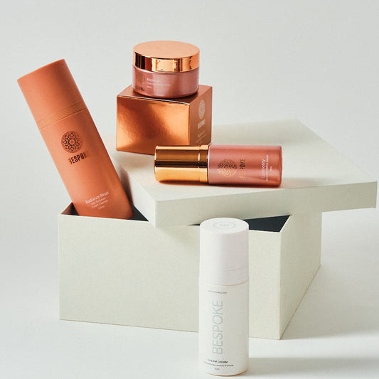 Set of skincare products including a white bottle, a brown jar, and a pink tube on a light background.